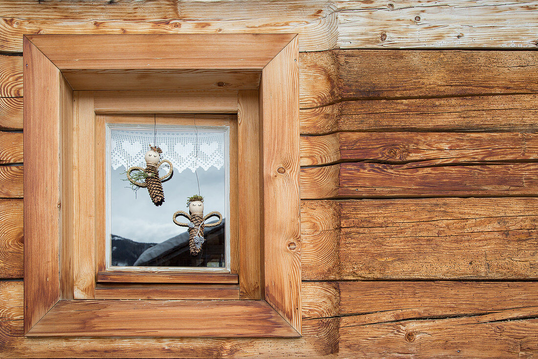 Engel aus Tannenzapfen im Fenster eines rustikalen Holzhauses