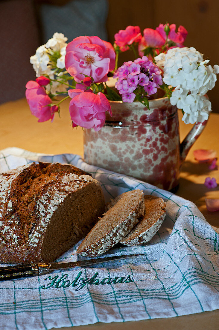 Bouquet of roses and phlox in jug and sliced bread on cloth