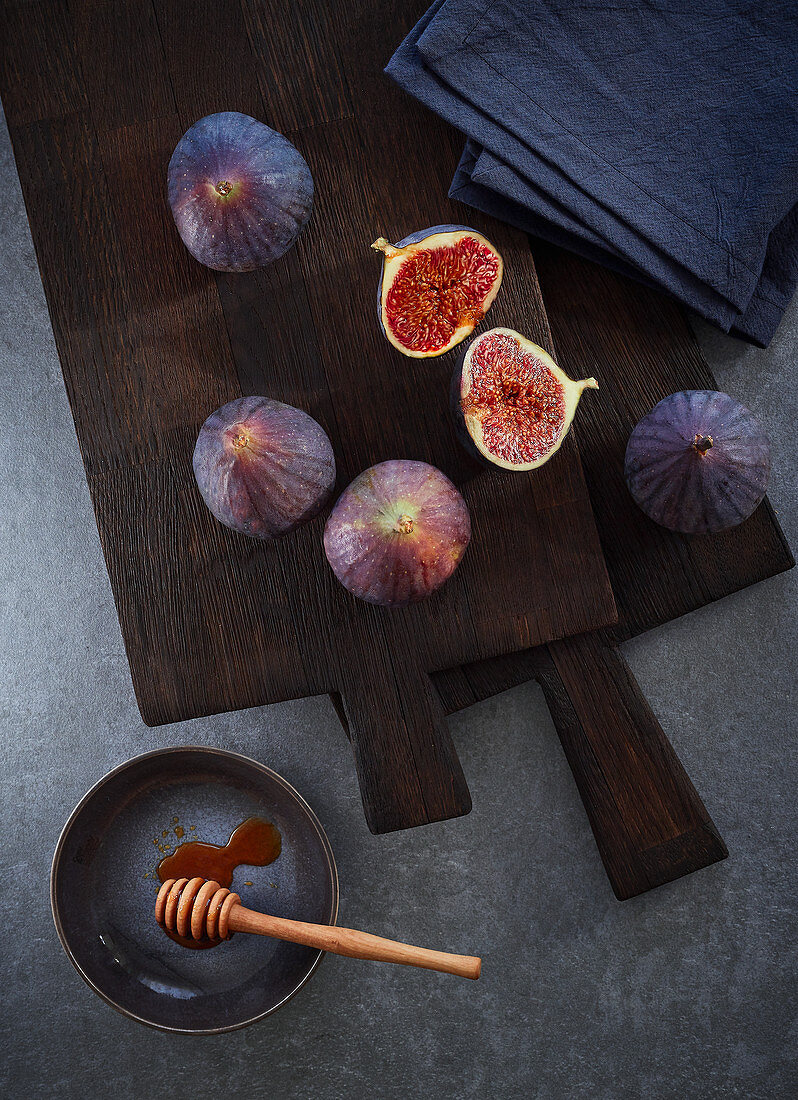 Fresh figs on a dark cutting board with a honey dipper