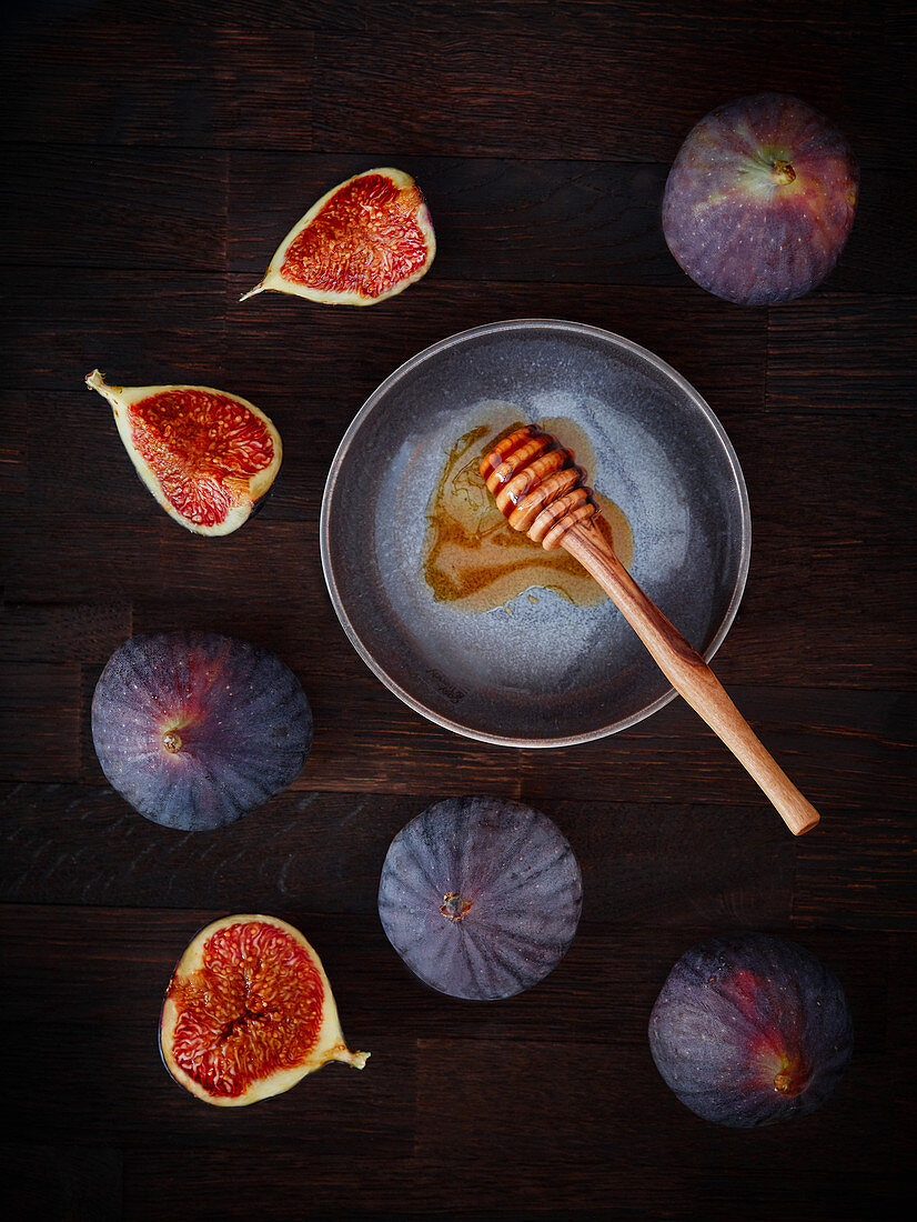 Fresh figs and a honey dipper on a dark wooden background
