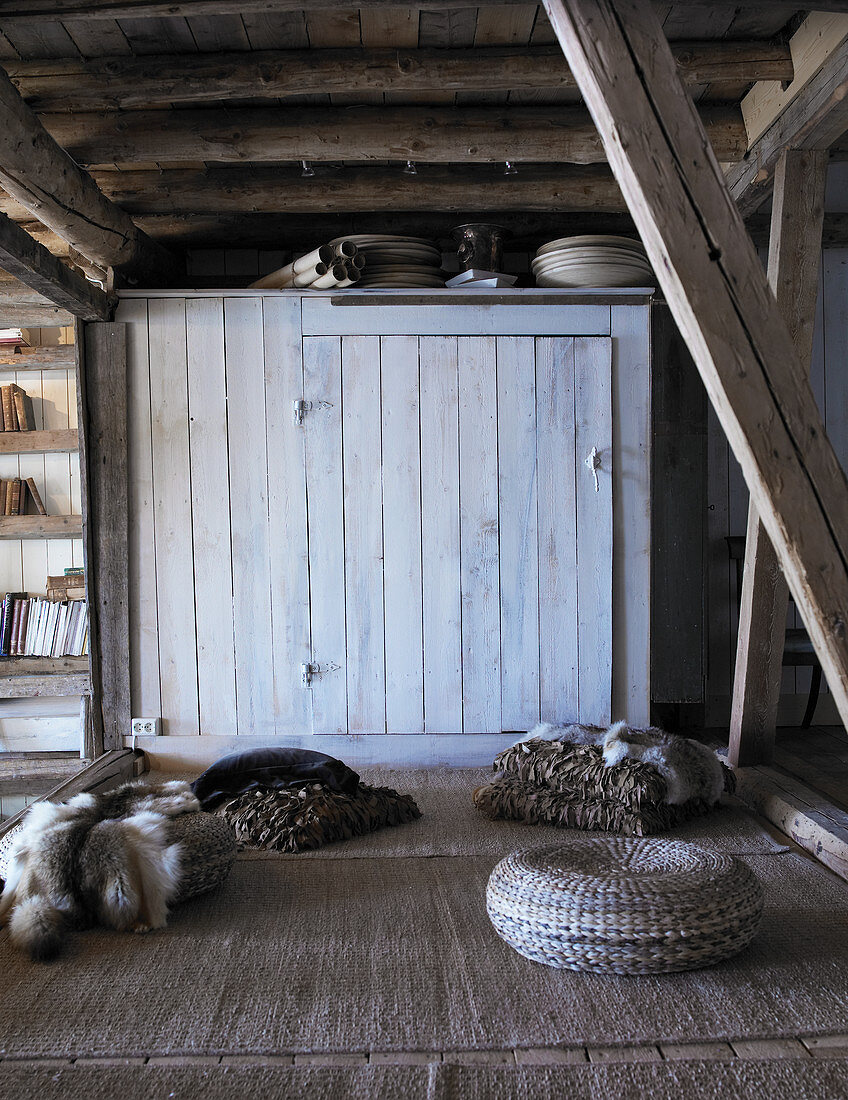 Floor cushions, fur blankets and pouffe in old, rustic wooden house