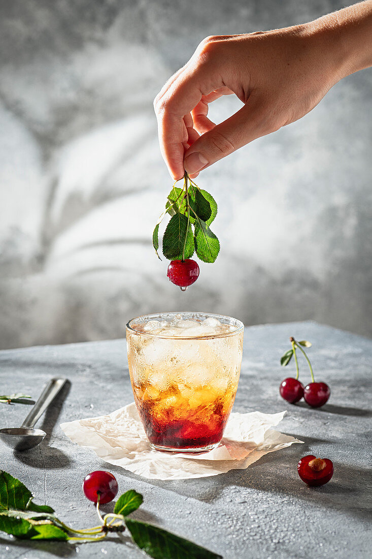 Iced Cherry Mocktail, darüber Hand mit Kirsche