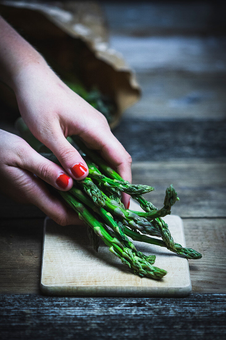 Women’s hands put green asparagus on a cutting board