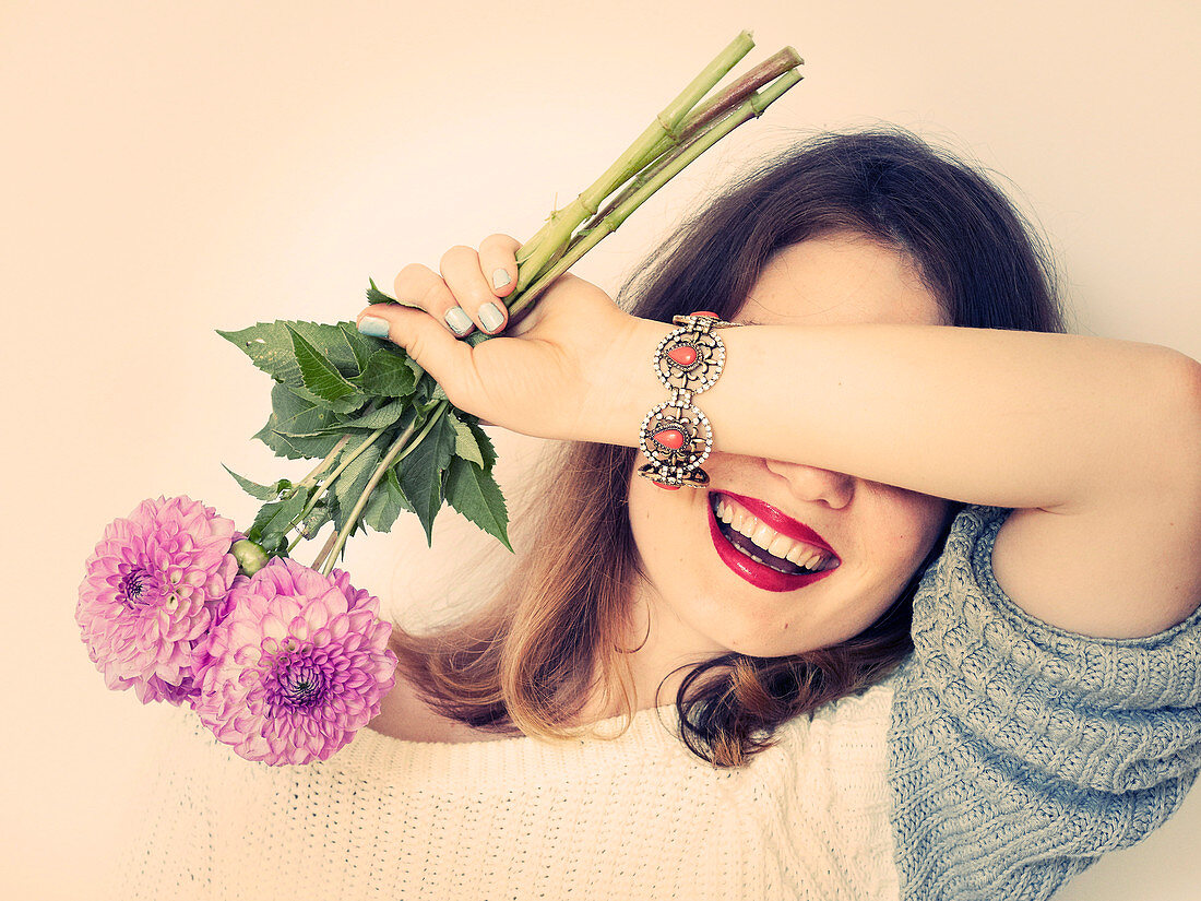 A woman holding a bunch of dahlias with her arm over her eyes