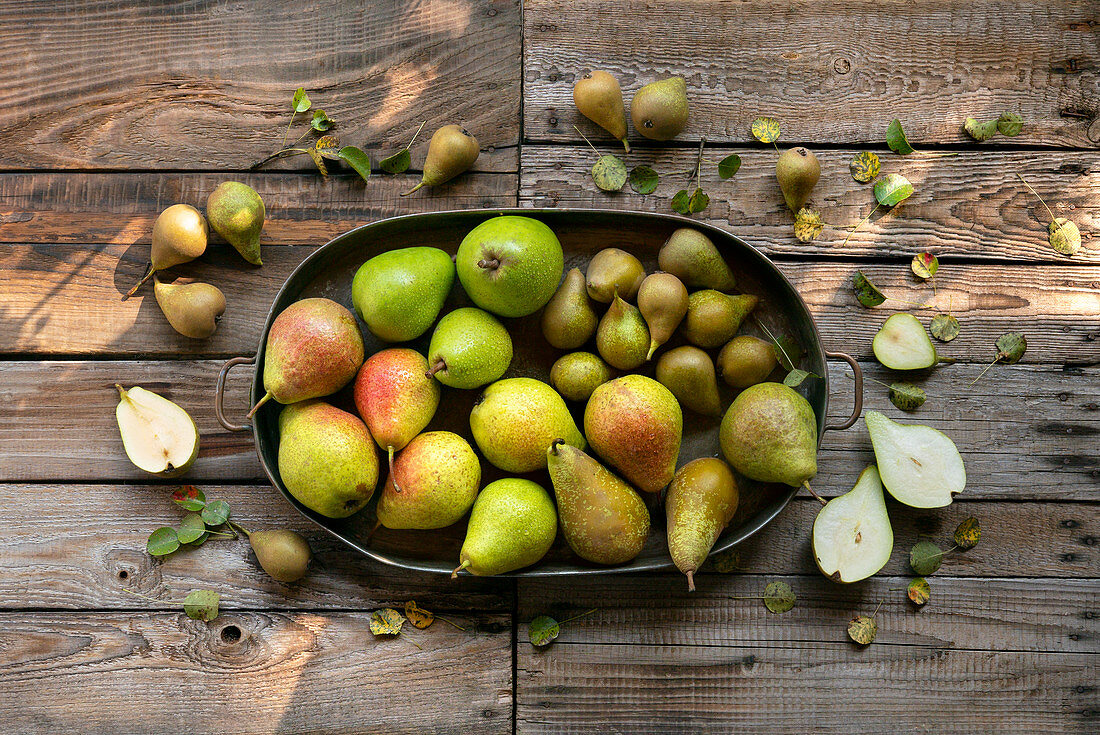 A composition of different kinds of pears on a wooden table top in the garden.