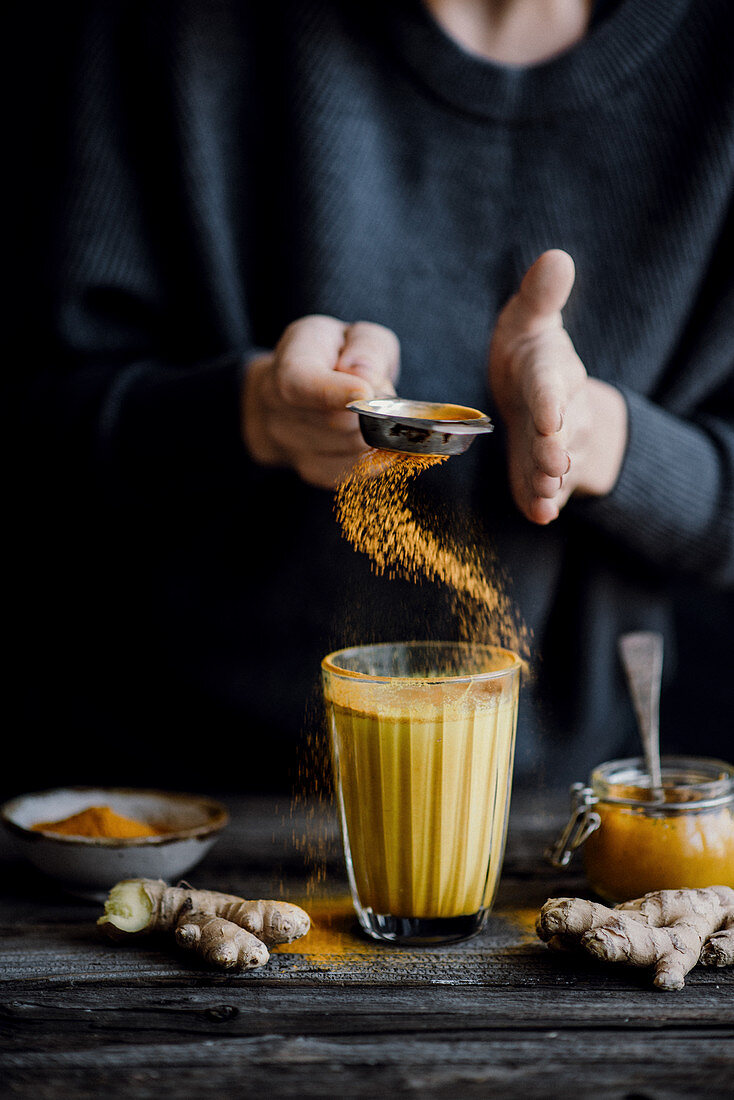 A person holding a glass of golden milk with turmeric ginger and honey