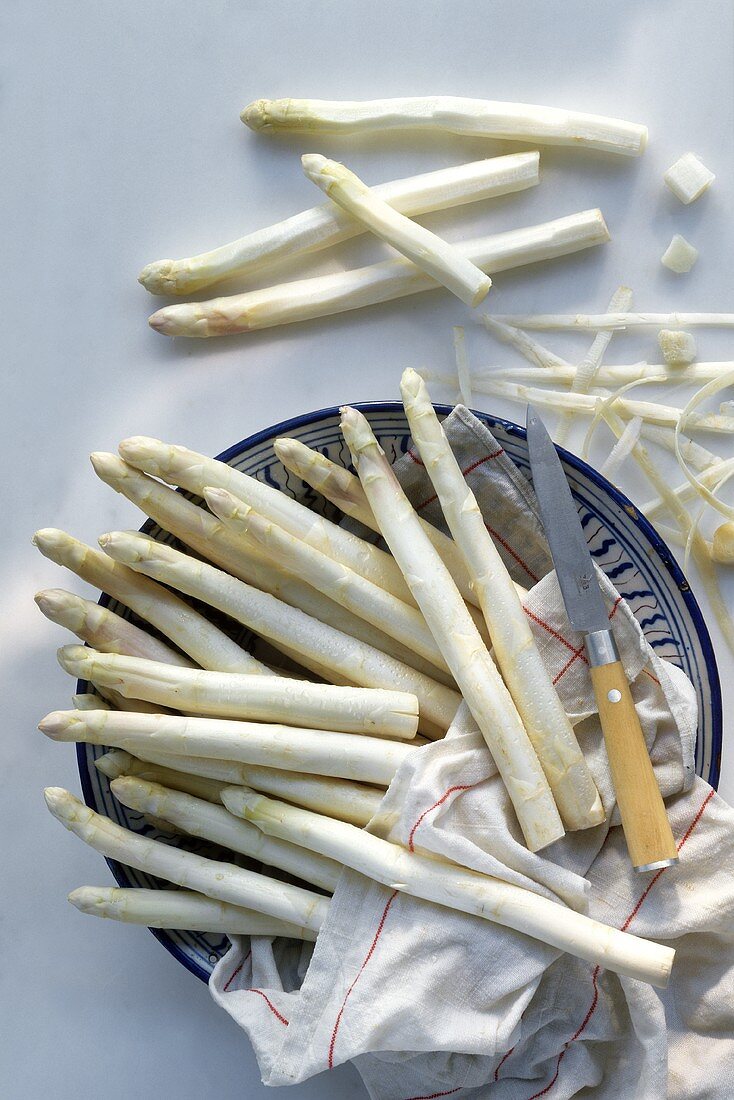 White asparagus spears in china bowl, peeled spears beside it