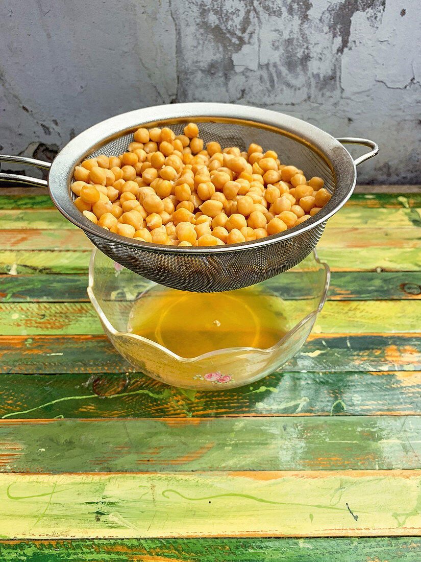 Draining soaked chickpeas in a glass bowl (aquafaba)