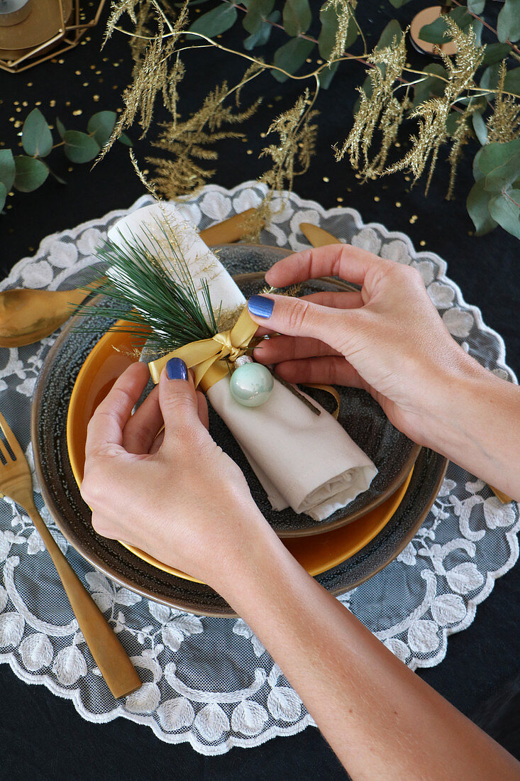 Hands tying decorations around napkin on set dining table