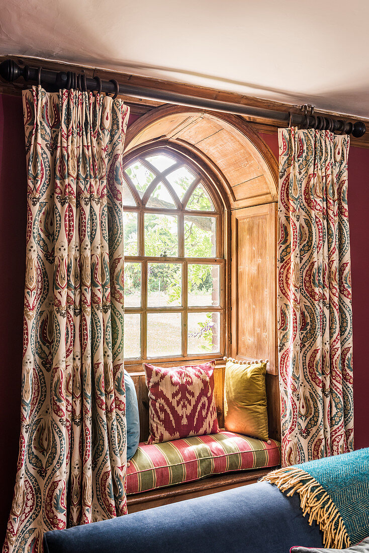 An arched window with a window seat and 1930s Art Deco-style curtains