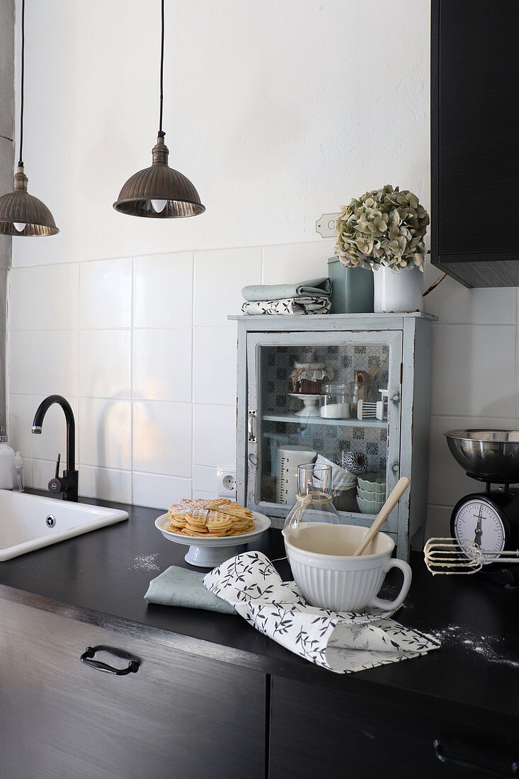 Baking utensils on worksurface in front of small glass-fronted cabinet