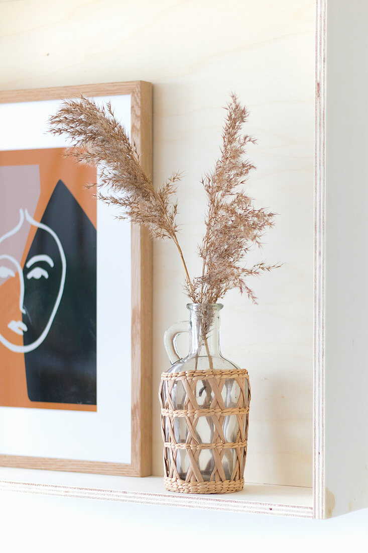 Pampas grass in wine bottle in basket standing on wooden frame