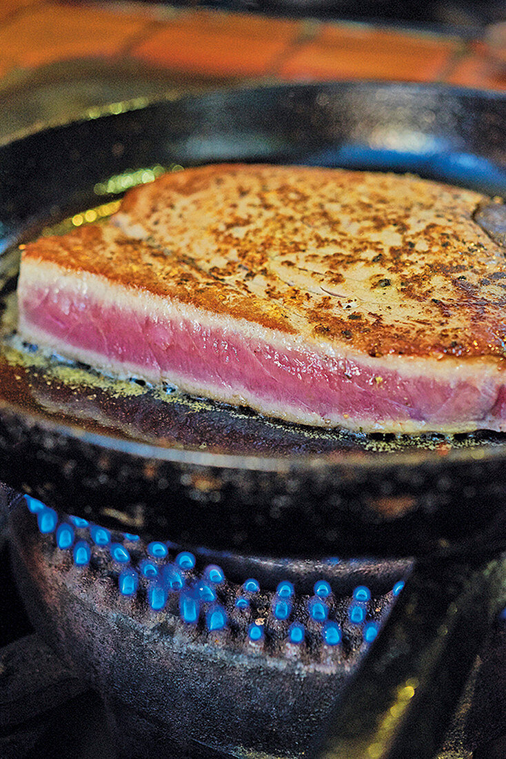 A tuna steak being fried in a pan