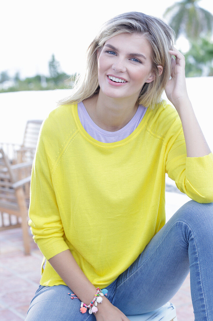 A young blonde woman wearing a yellow jumper and jeans