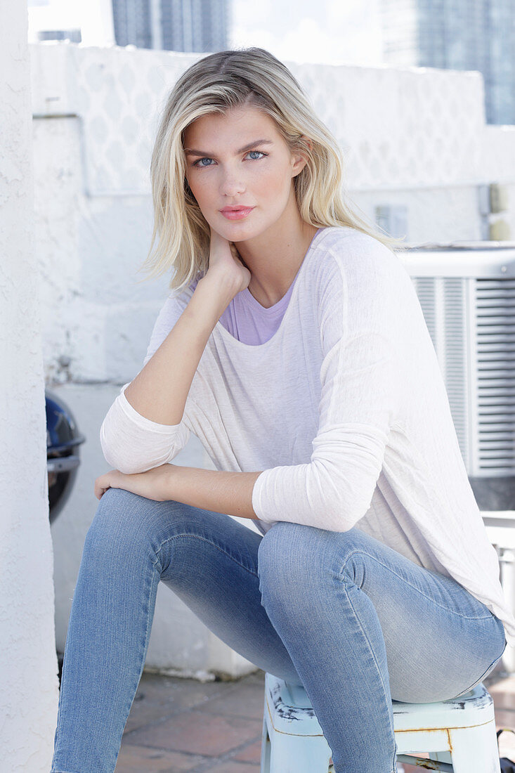 A young blonde woman wearing a purple t-shirt and a white jumper