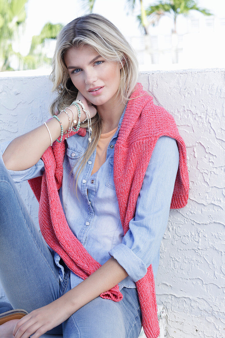 A young blonde woman wearing a denim shirt with a coral-coloured jumper over her shoulders