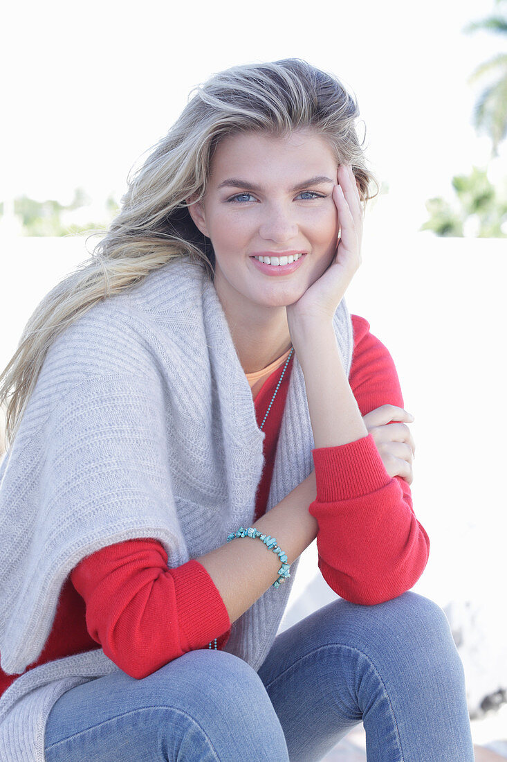 A young blonde woman wearing a red jumper with a light-coloured jumper over her shoulders