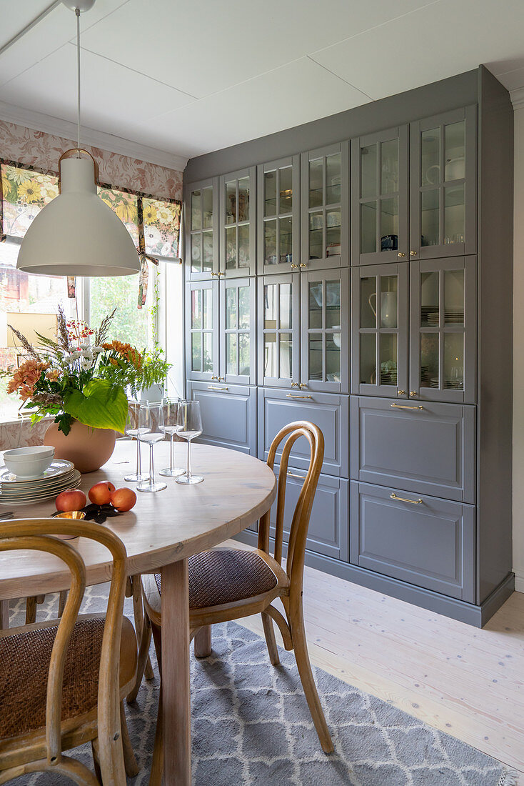 A grey lacquered cabinet and a round wooden dining table in a kitchen