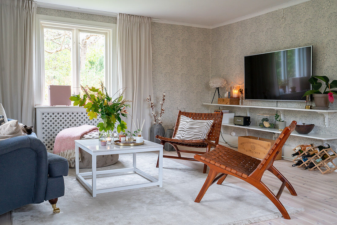 A designer armchair made of wood and leather in a living room with patterned wallpaper