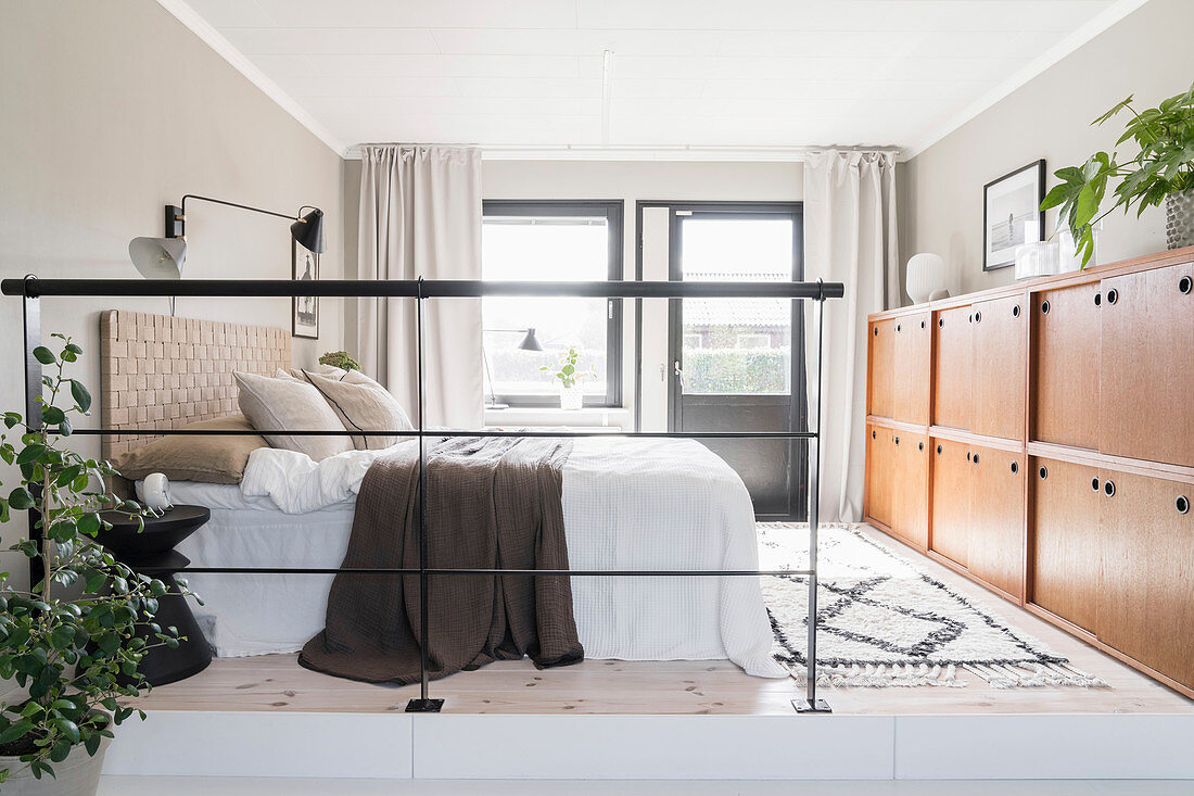 A double bed and a half-height cupboard in a sleeping area with an iron railing as a room divider