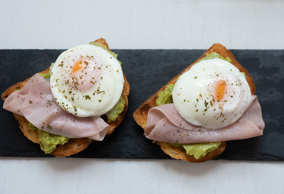 Appetizing toasts with guacamole garnished with tasty fried eggs and ham placed on table for breakfast