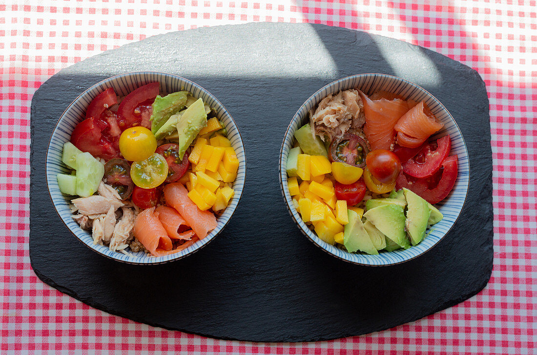 Top view of bowls with chopped fresh vegetables and meat of salmon and chicken placed on table in kitchen for lunch