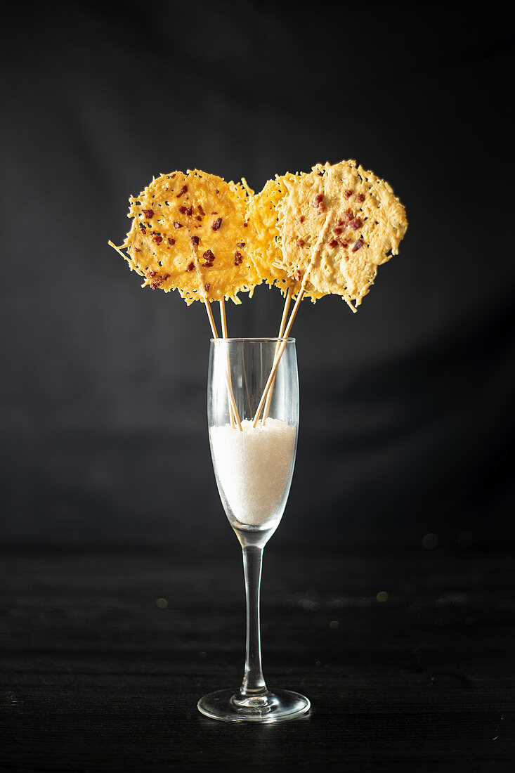 Glass with rice for decoration of crispy grated cheese chips on sticks placed on black background