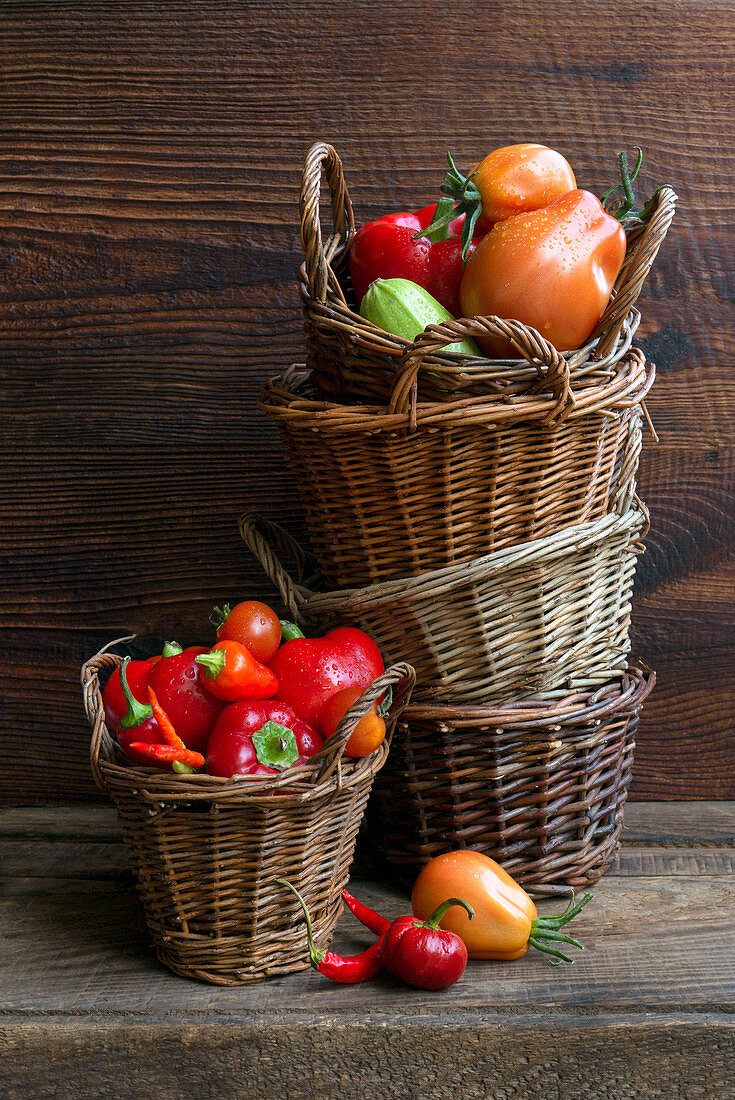 Paprika und Tomaten in Weidenkörben auf Holztisch