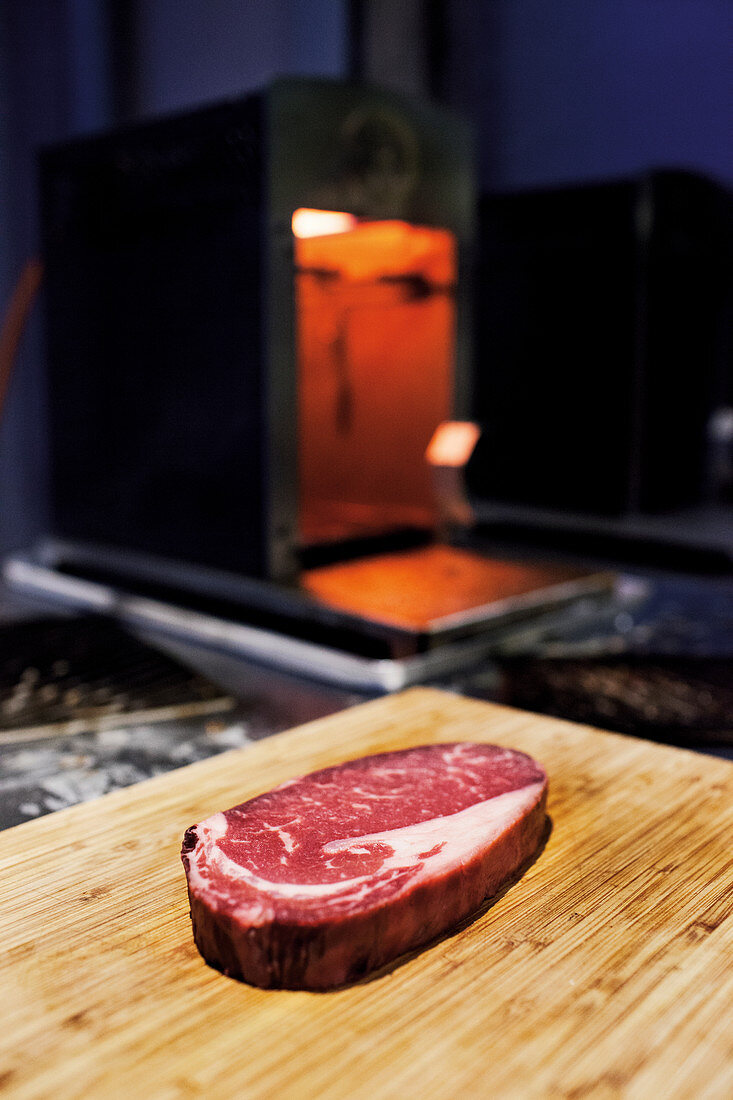 A raw steak on a wooden board in front of a Beefer