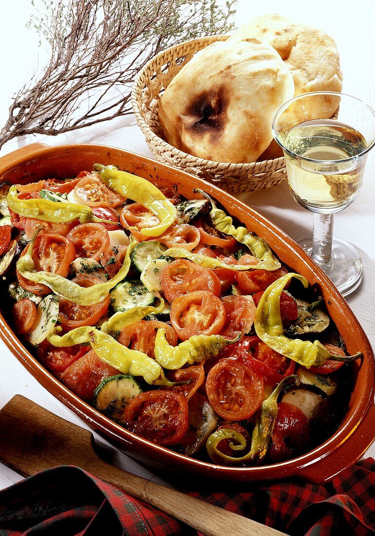 Greek vegetables in clay bowl; 2 pita breads in bread basket