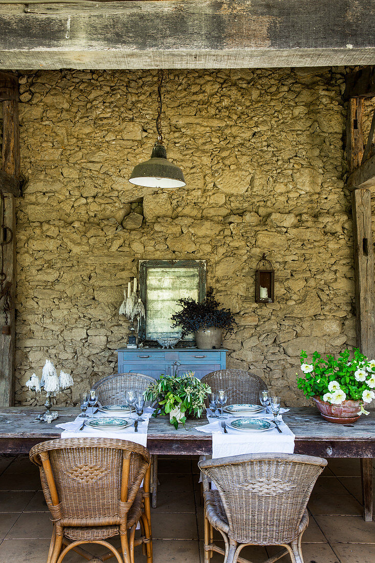 Long dining table with rattan chairs on the veranda of a stone house