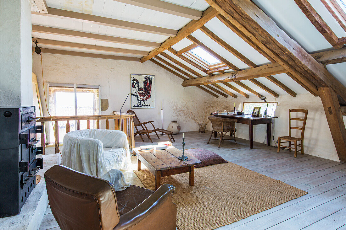 Armchair and wooden table in rustic attic bedroom with wood-beamed ceiling