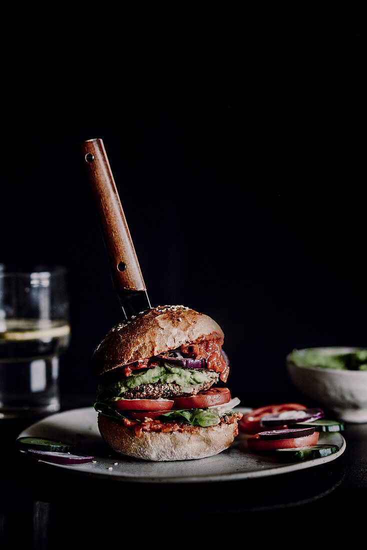 Veganer Burger auf Teller vor schwarzem Hintergrund