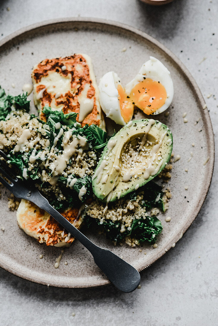 Millet with avocado kale egg and grilled halloumi topped with tahini sauce