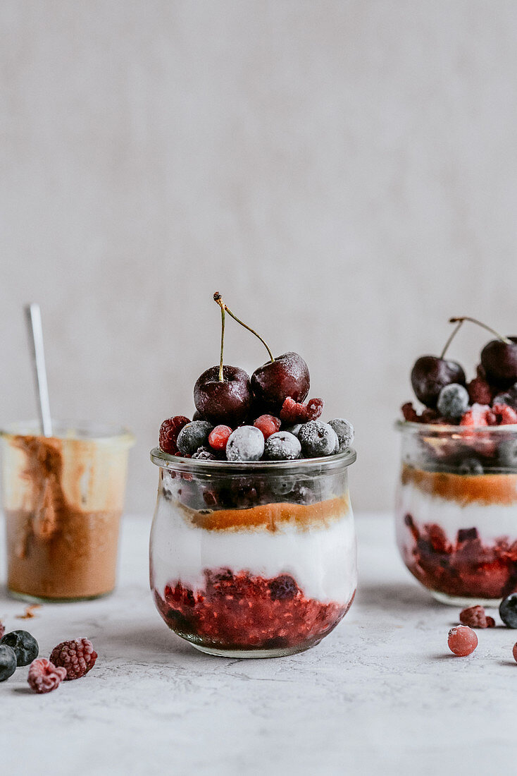 Schichtdessert im Glas mit gefrosteten Beeren, Kirschen und Erdnussbutter