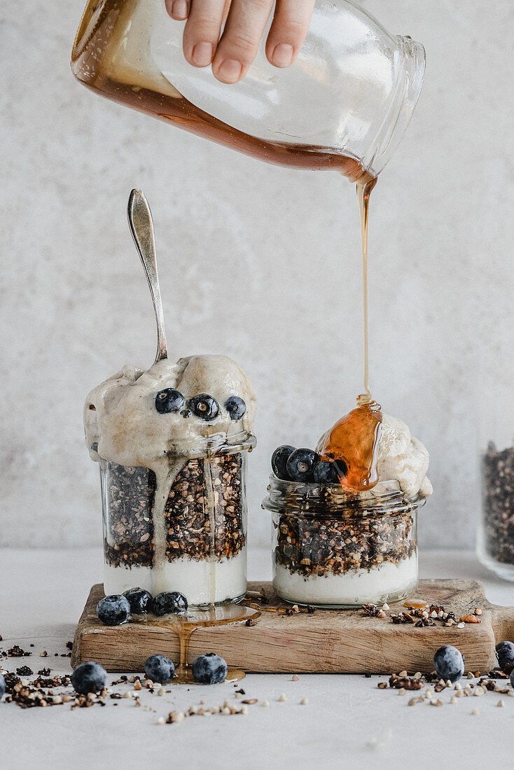 Granola with yogurt in a jar with blueberries banana ice cream topped with maple syrup