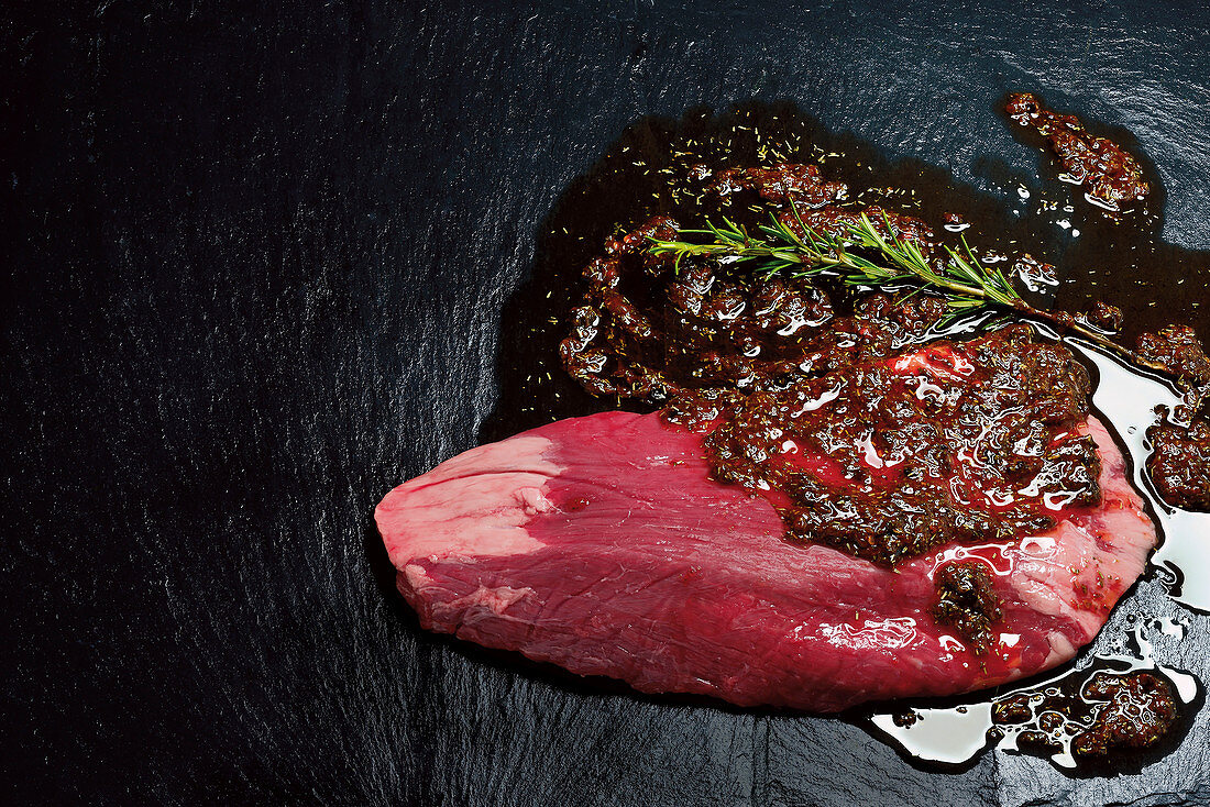 Raw flank steak with marinade on a dark background