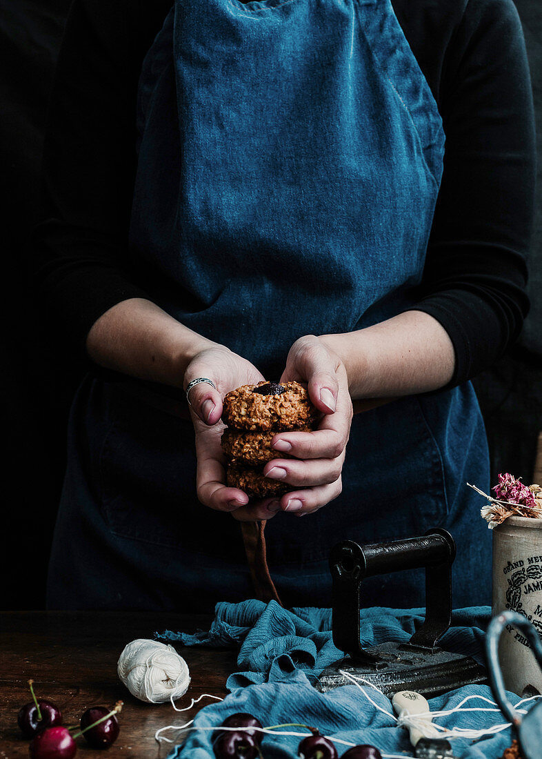 Hand with stack of cookies at table with fresh cherry and retro iron on cloth