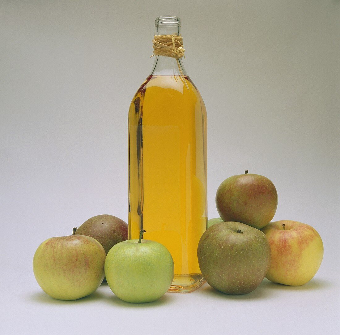 Eine Flasche Apfelessig, Deko: sechs frische Äpfel