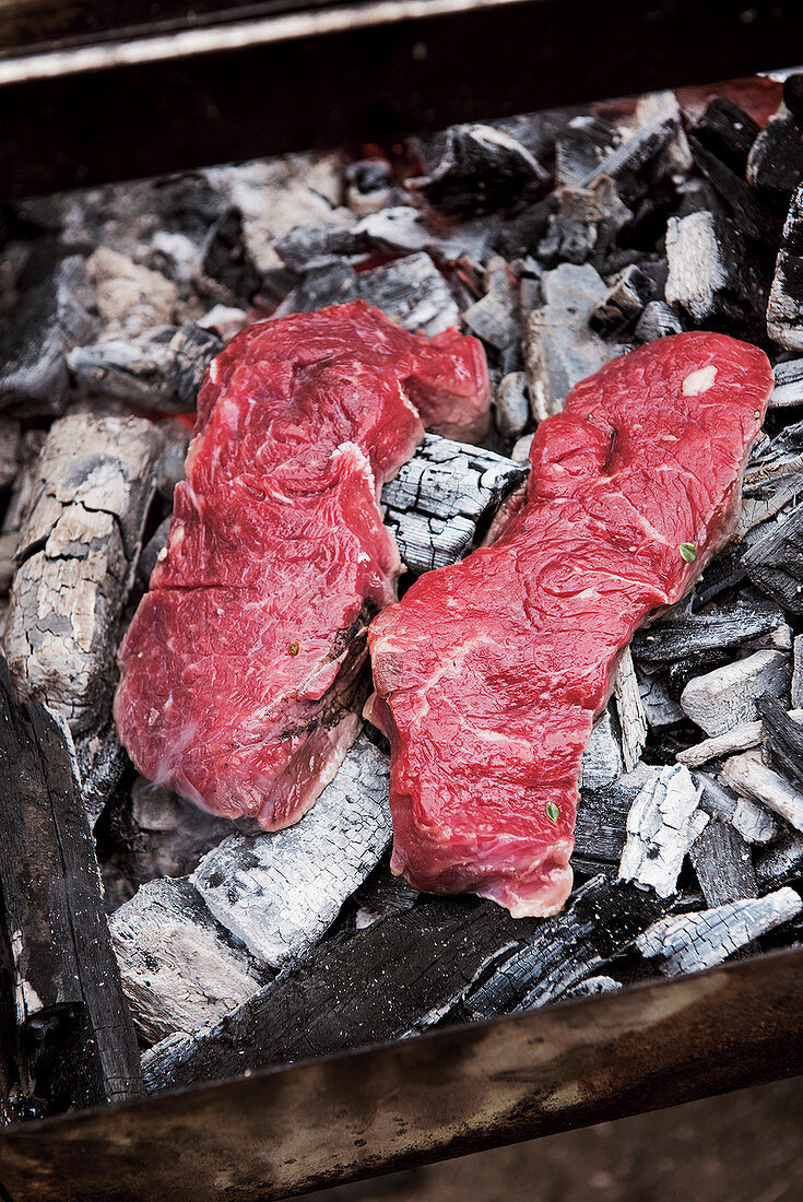 Raw steaks being grilled in hot coals