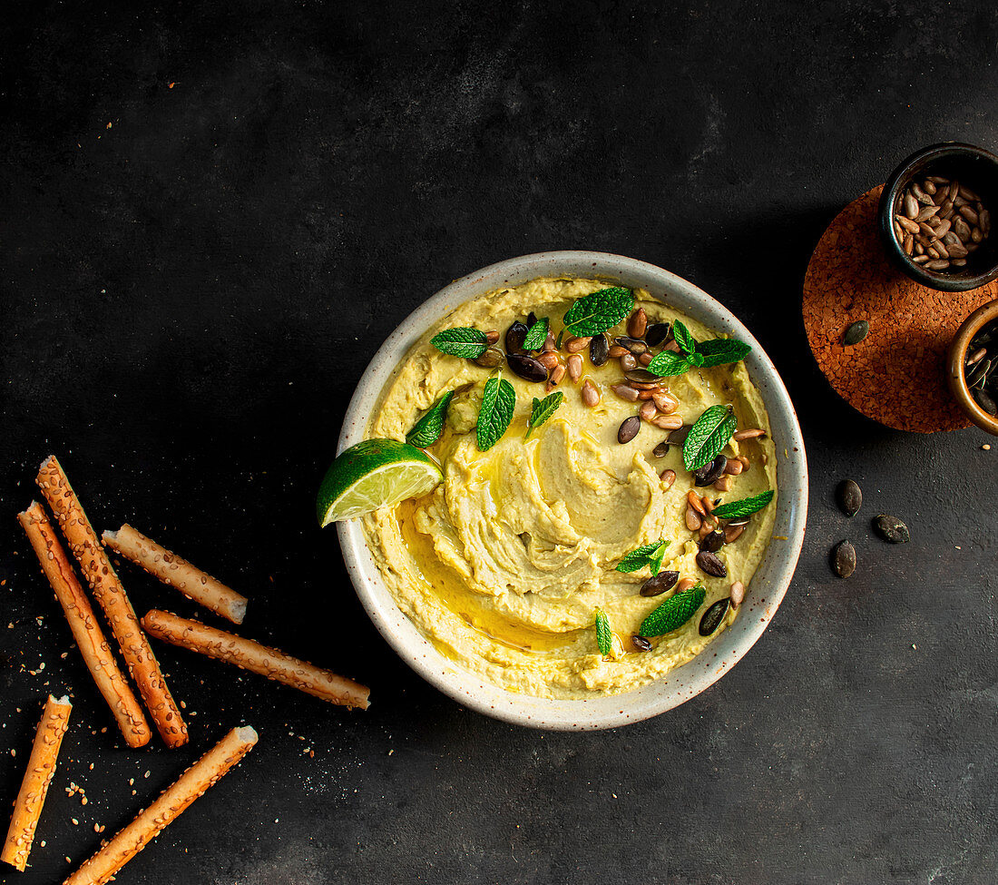 Hummus peas placed on a bowl near crackers on dark background