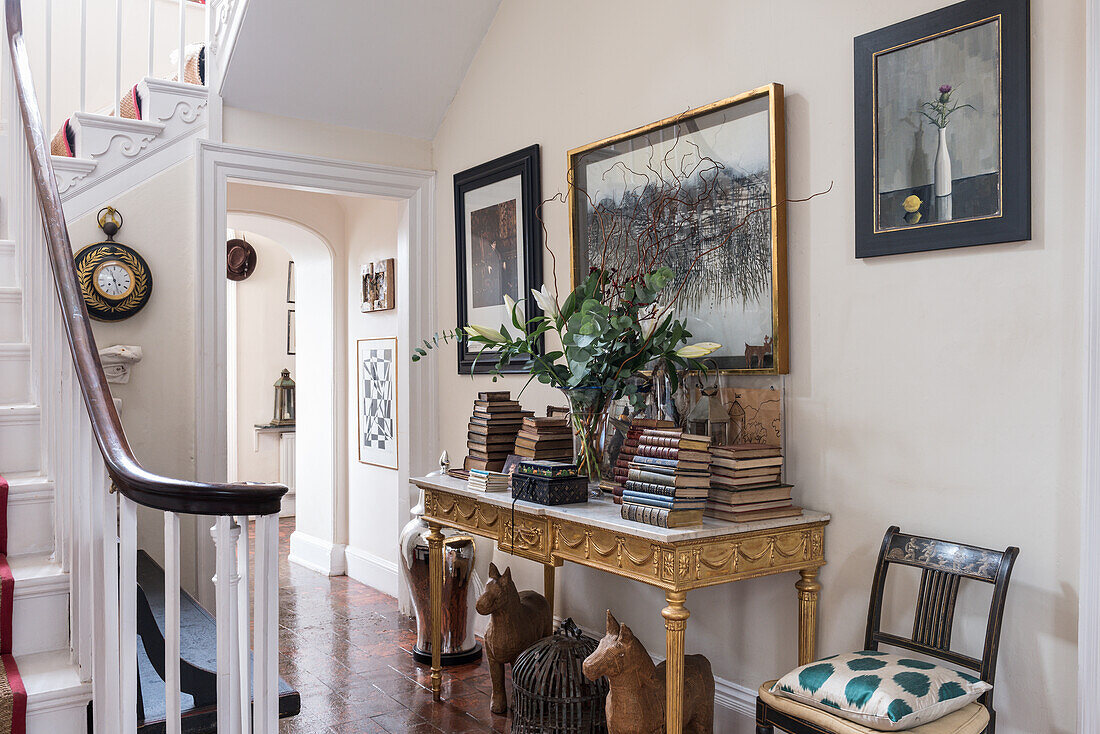 Neatly stacked books on neoclassical gilded table in front hall with hand painted, lacquered 19th century French chairs