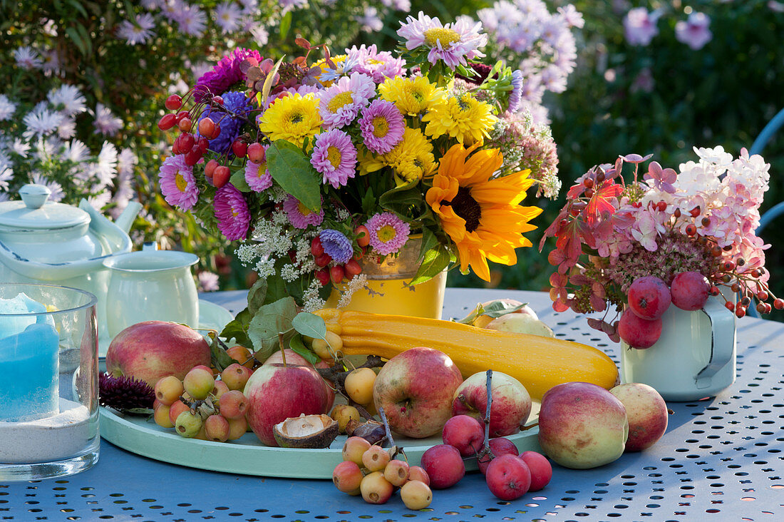 Colorful table setting with bouquets of chrysanthemums, summer asters, sunflower, hydrangea, sedum and crabapple, apples, and summer squash on a tray