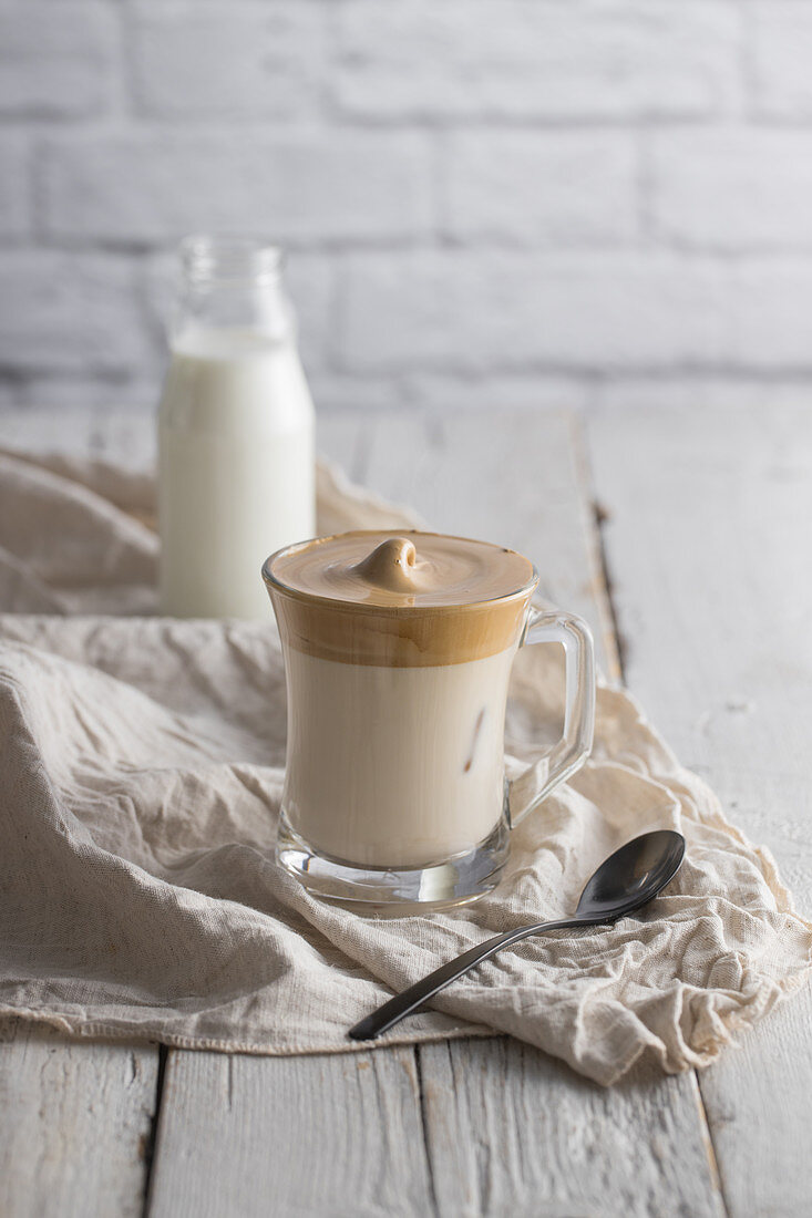 Cold homemade Dalgona beverage with whipped coffee placed on wooden table with bottle of milk and teaspoon