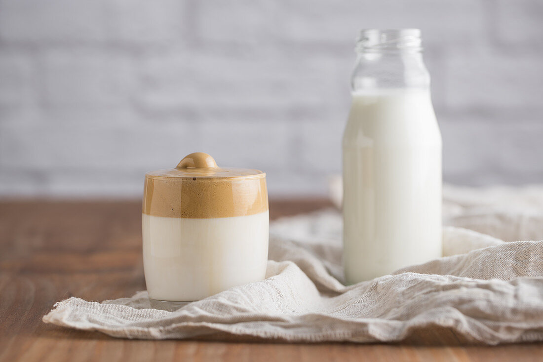 Cold homemade Dalgona beverage with whipped coffee placed on white napkin in wooden table with bottle of milk