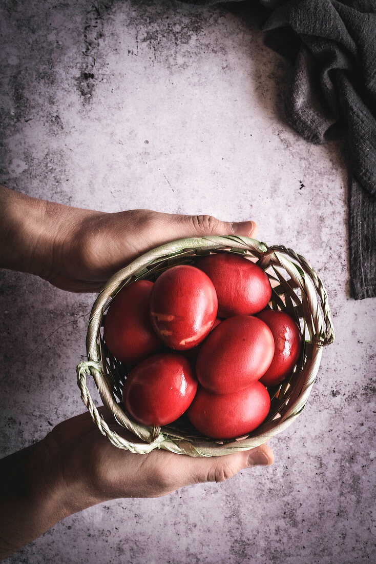 Hands holding basket with red eggs