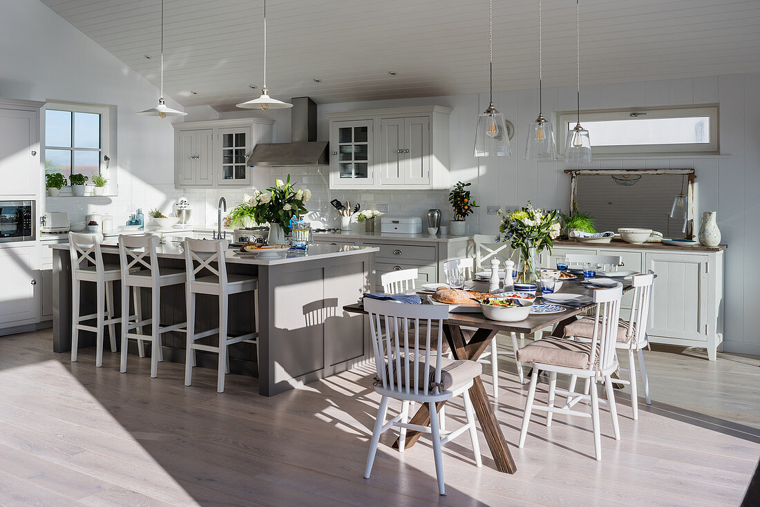 Open plan kitchen and dining room with sea views Bar stools at island unit with dining table and chairs in sunlit coastal home