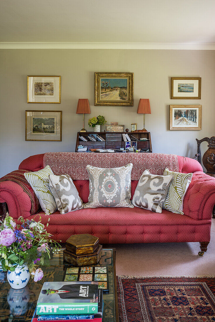 Couchtisch, pinkfarbenes Sofa mit Kissen und Bilder an der Wand im Wohnzimmer