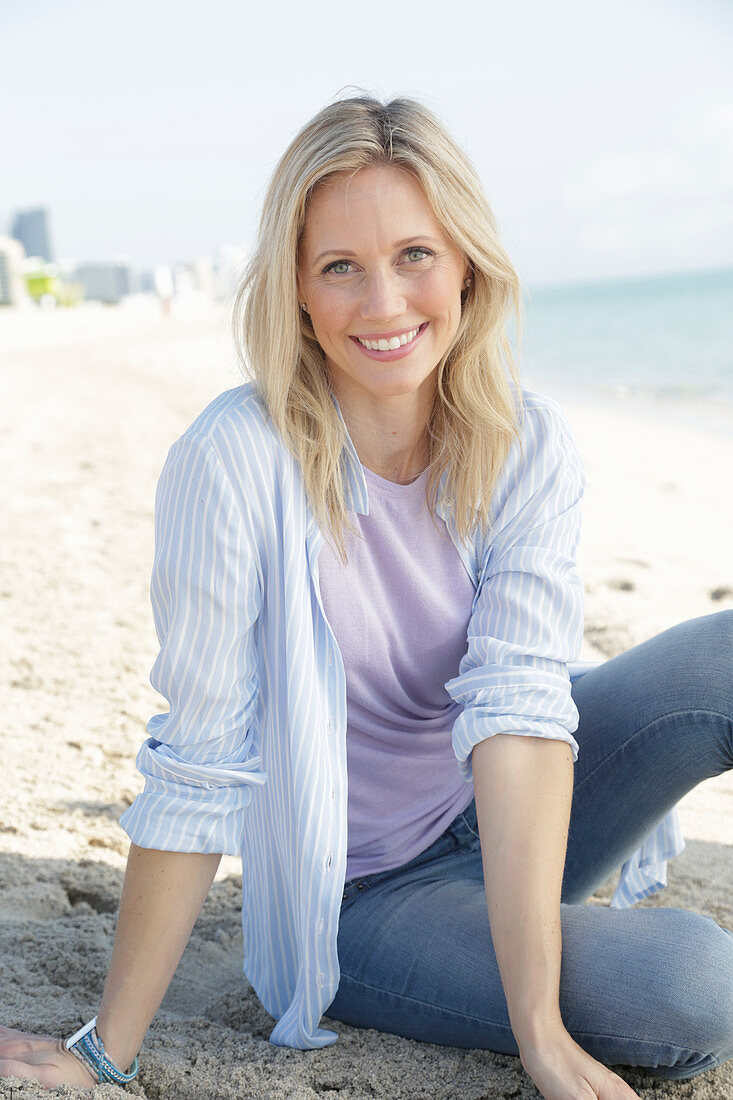 Blonde Frau in blau-weiß gestreiftem Hemd und Jeans am Meer