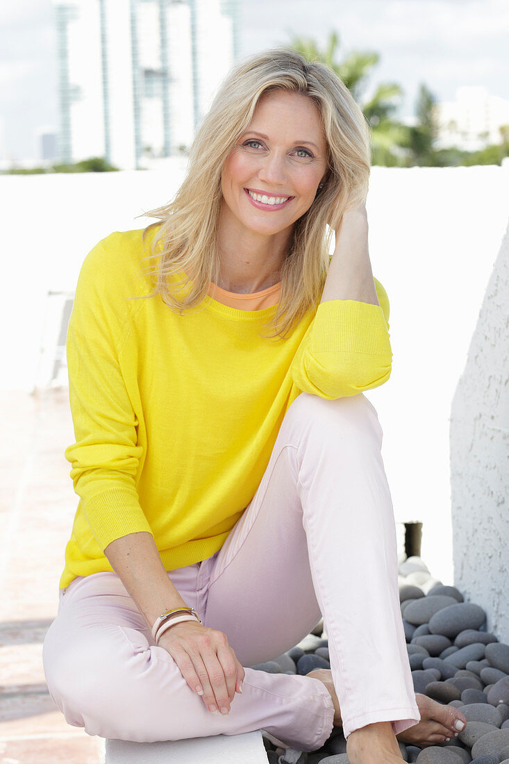 A blonde woman wearing a yellow jumper and white trousers